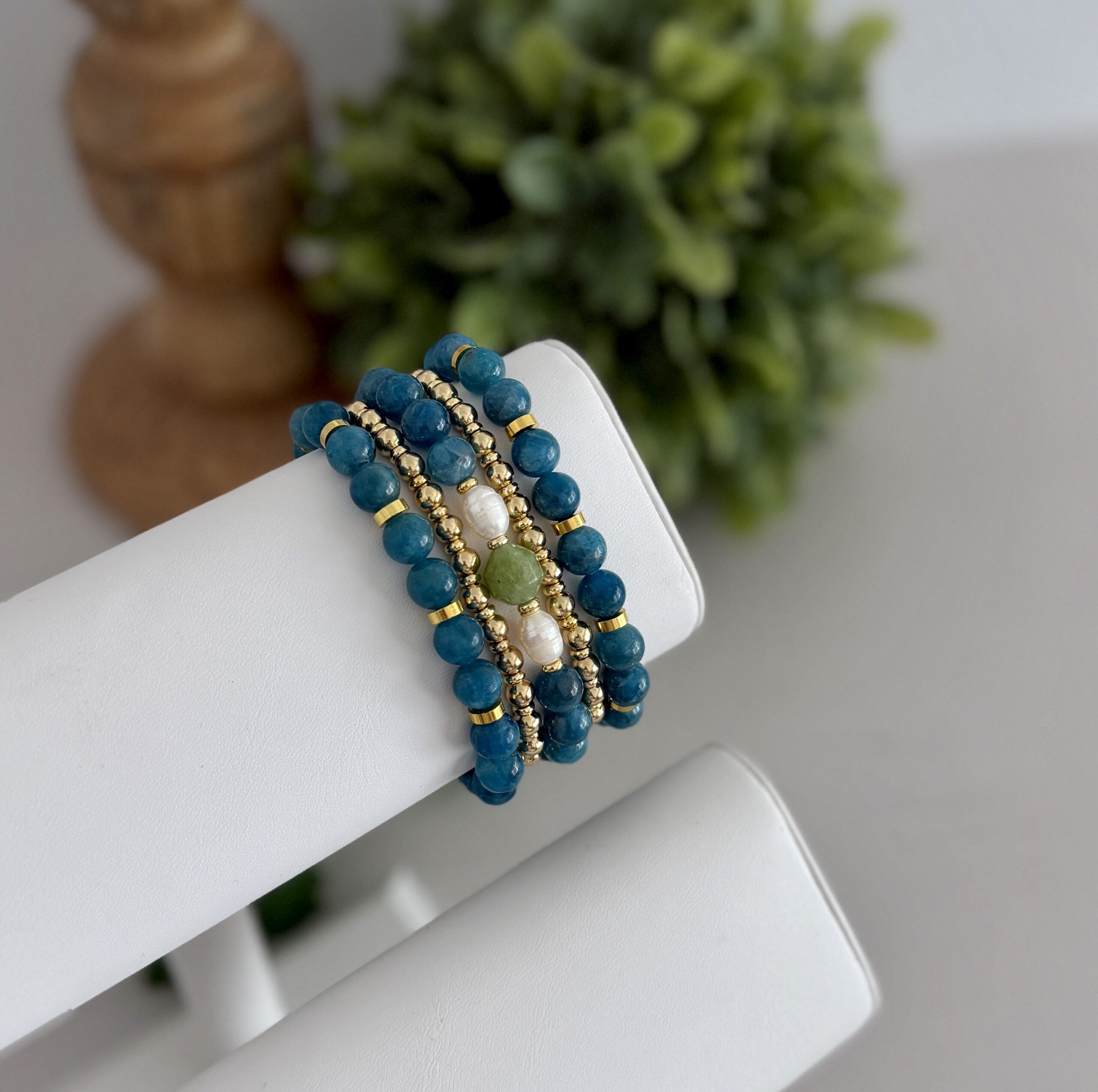 Deep teal blue apatite gemstone bracelet. This has several matching styles. One uses pearls and a touch of green. They are paired with two gold tone stretch bracelets to create a stack