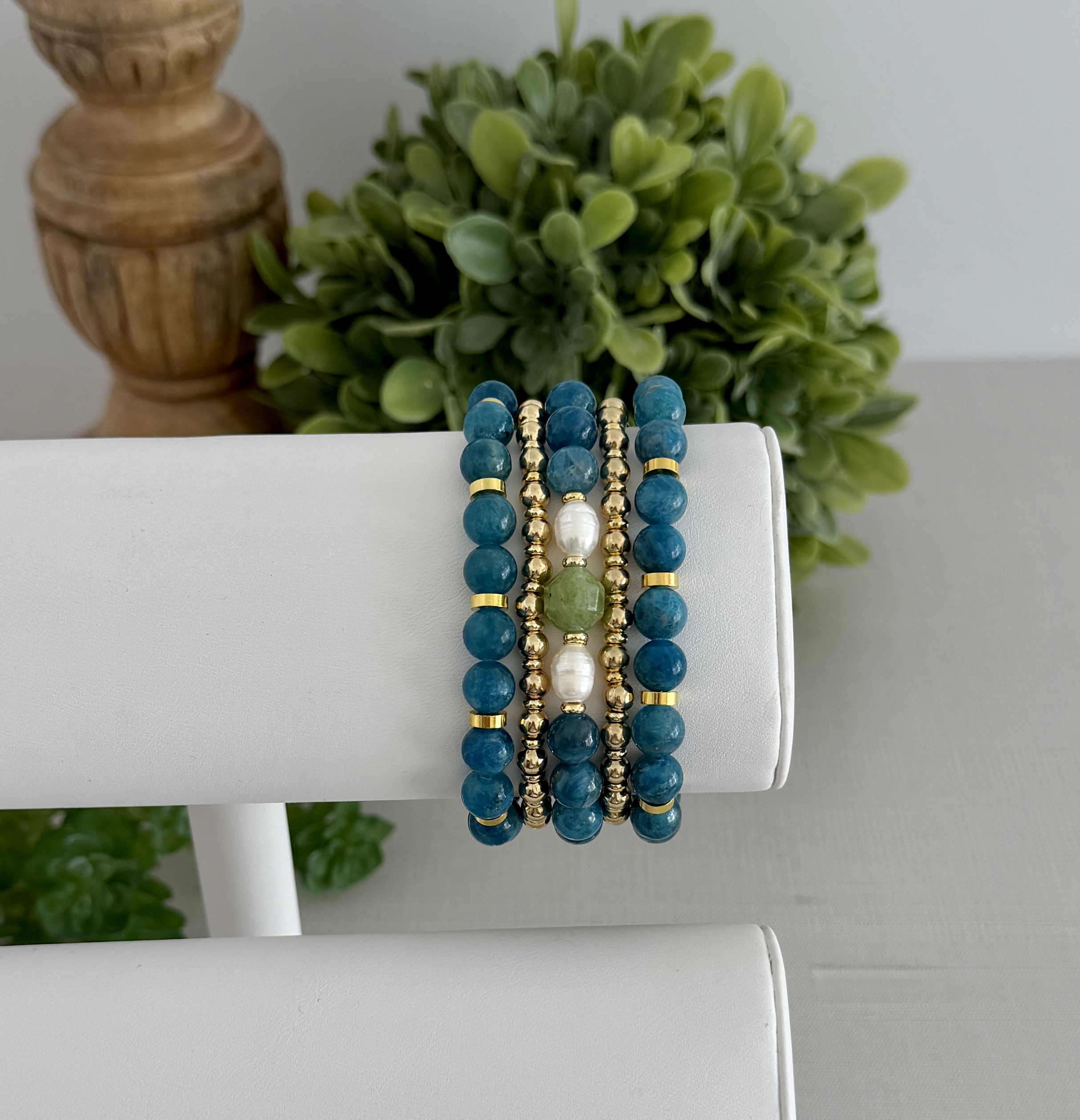 Deep teal blue apatite gemstone bracelet. This has several matching styles. One uses pearls and a touch of green. They are paired with two gold tone stretch bracelets to create a stack