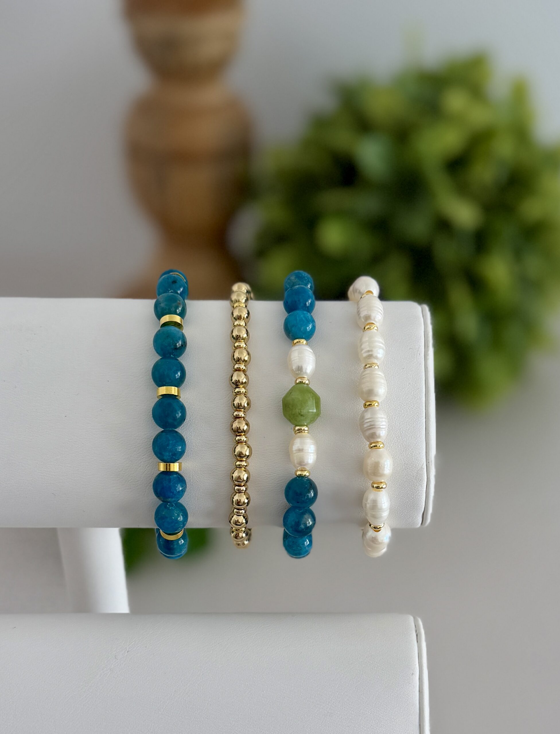 Deep teal blue apatite gemstone bracelet. This has several matching styles. One uses pearls and a touch of green. They are paired with two gold tone stretch bracelets to create a stack