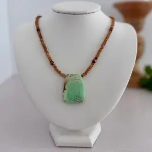 A large green varisite stone pendant sits centered on the hessonite garnet necklace. The length is 17” and the clasp is a lobster style closure.