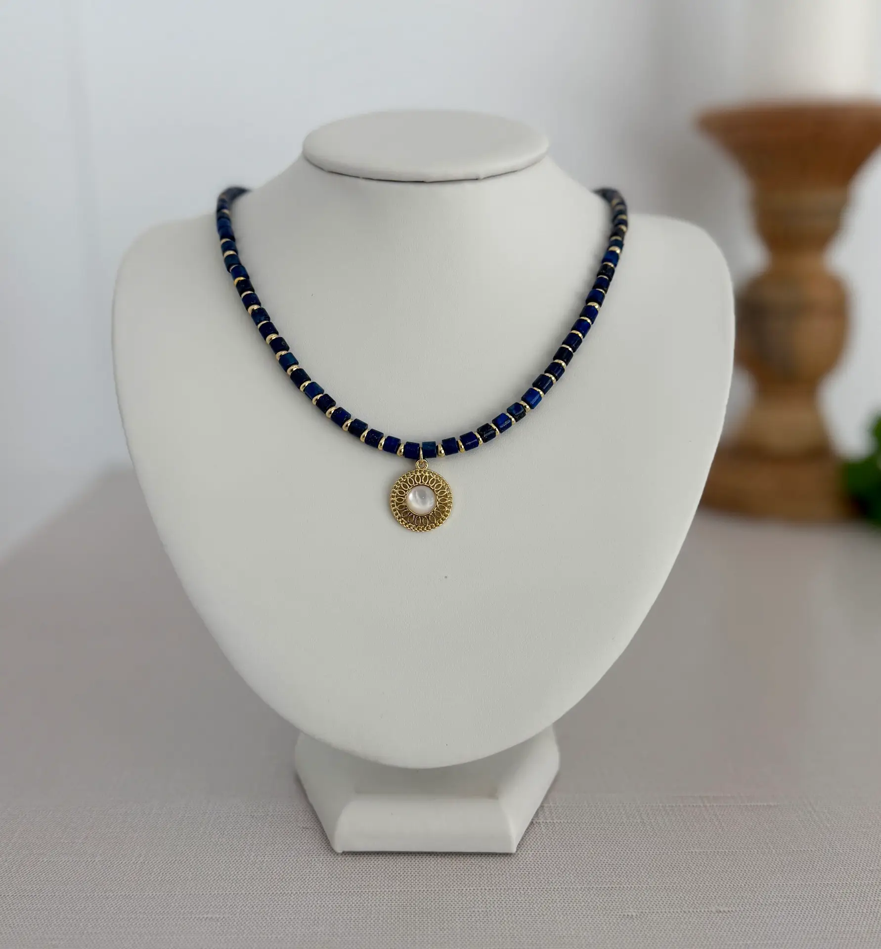 Blue lapis lazuli beads separated by gold disk spacers. 16” with a round gold and moonstone medallion in the center. The clasp is a lobster style closure